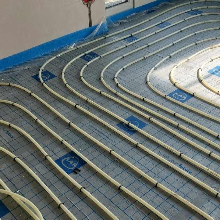 Układanie rur systemu ogrzewania podłogowego na izolacji z siatką, widoczne mocowania rur do podłoża oraz fragment ściany i okna.