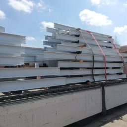 WOBISTAL WB SP. Z O.O. - Białe, stalowe belki konstrukcyjne, zabezpieczone pasami transportowymi, ułożone na platformie ciężarówki, gotowe do przewozu na plac budowy.