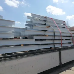 Białe, stalowe belki konstrukcyjne, zabezpieczone pasami transportowymi, ułożone na platformie ciężar&oacute;wki, gotowe do przewozu na plac budowy.