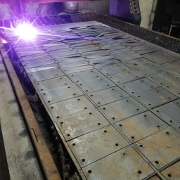 WOBISTAL WB SP. Z O.O. - Automatyczna wycinarka plazmowa tnie arkusz blachy na kwadratowe elementy z otworami, widoczne iskry i ciemne otoczenie hali produkcyjnej.