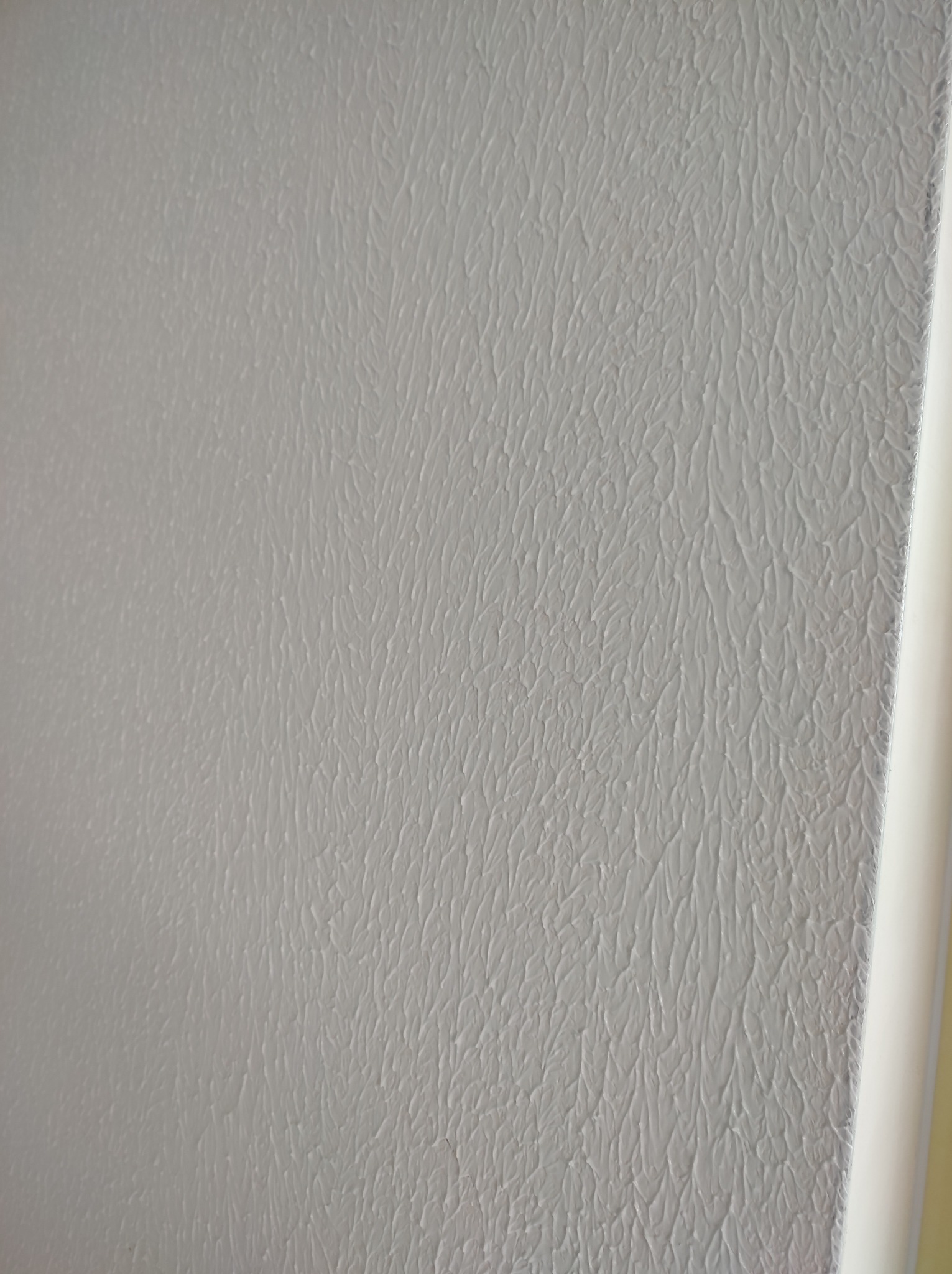 Szara ściana z fakturą baranka, wykonana w Warszawie, z widocznym fragmentem białej listwy przypodłogowej w prawym rogu.