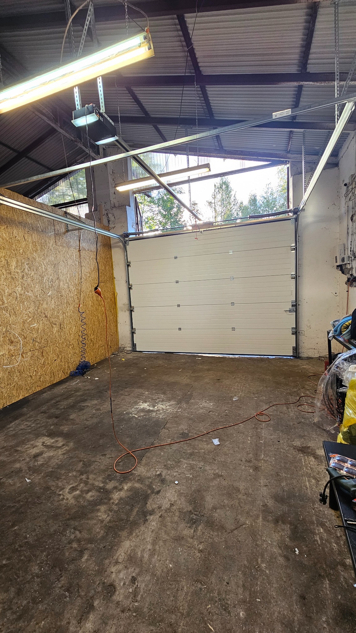 Zamknięta, segmentowa brama garażowa w jasnym kolorze, zamontowana w garażu z surowymi ścianami i betonową podłogą, widoczny napęd bramy pod sufitem.