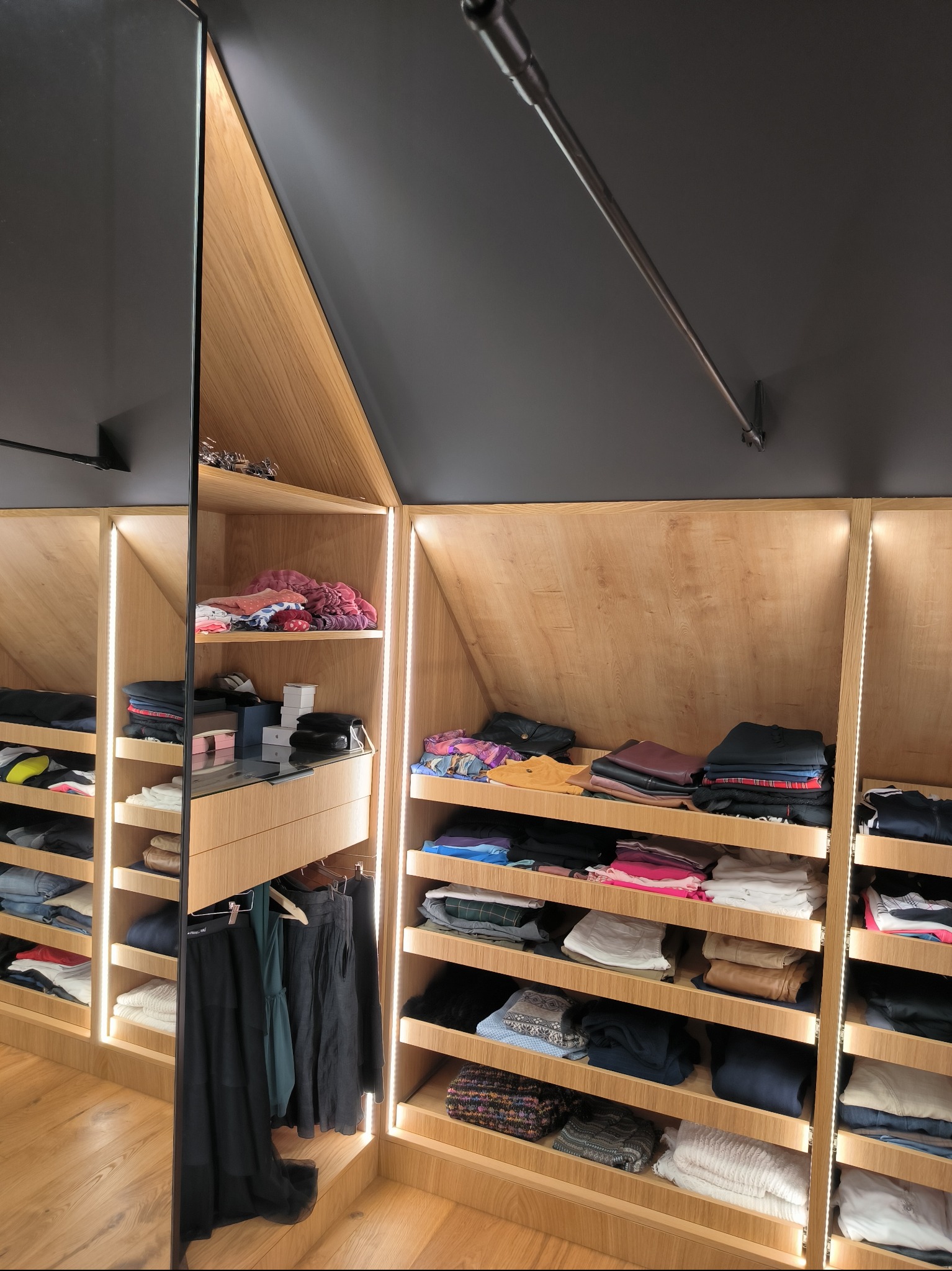 Szafa wnękowa na poddaszu we Wrocławiu, z oświetleniem LED, półkami wypełnionymi ubraniami i lustrzanymi drzwiami.