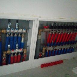 Hydro-Serwis - Rozdzielacz ogrzewania podłogowego w zabudowie z rurami w kolorze czerwonym i niebieskim, widoczne zawory i złączki