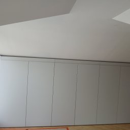 Rem-Pat - Nowoczesna zabudowa szafy wnękowej z matowymi, białymi frontami, sięgająca sufitu na poddaszu, widoczna z dołu.