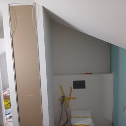 Rem-Pat - Łazienka w trakcie prac: obudowa z płyty karton gips, częściowo wykończone płytki, zabezpieczona taśmą toaleta, widoczne instalacje.