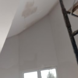 Rem-Pat - Nierównomiernie wyszpachlowany fragment sufitu pod skosem, widoczny fragment rusztowania i okna w tle.