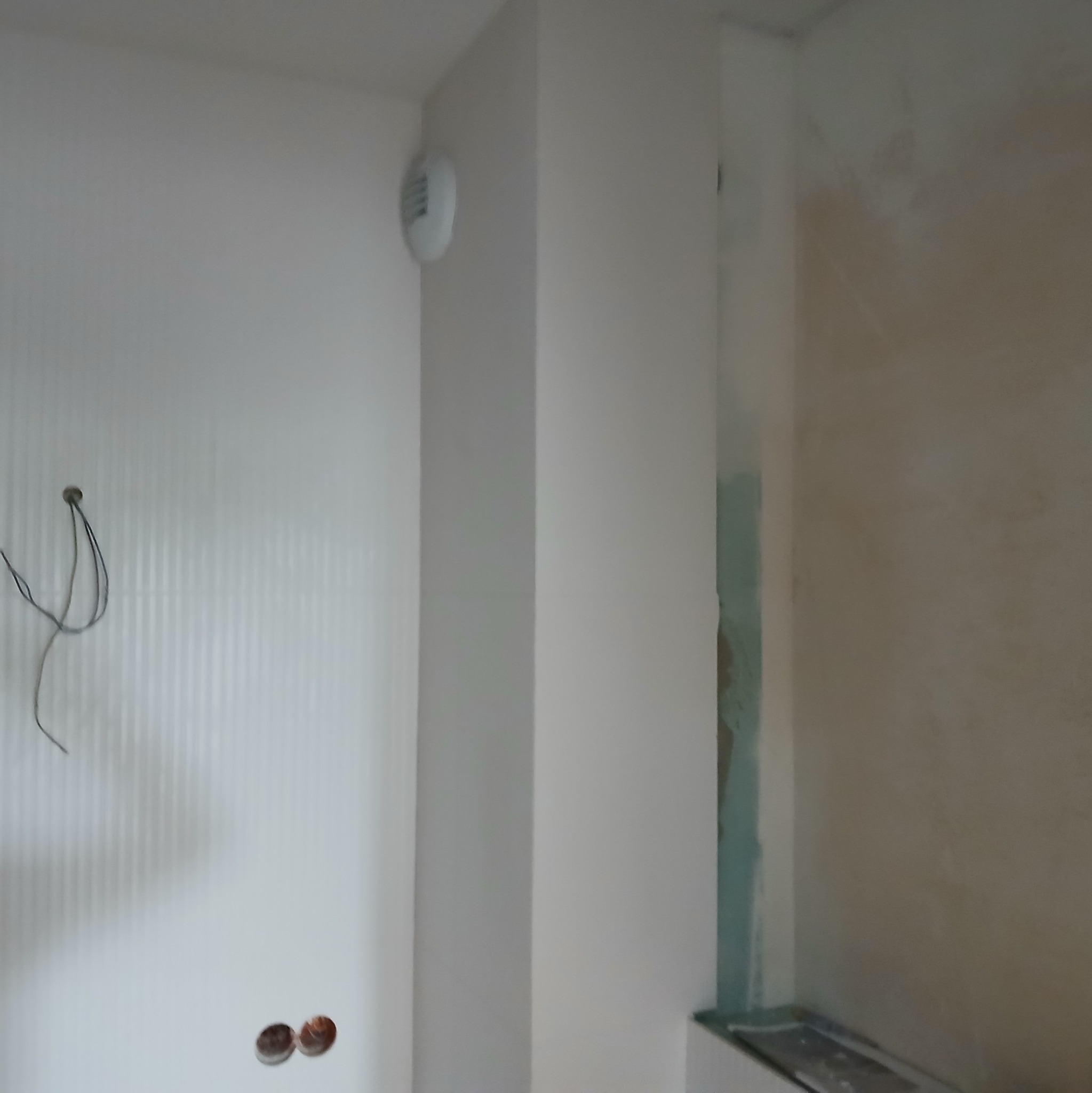 Fragment ściany w trakcie szpachlowania z widocznymi przewodami elektrycznymi, wentylacją i śladami po szpachli.