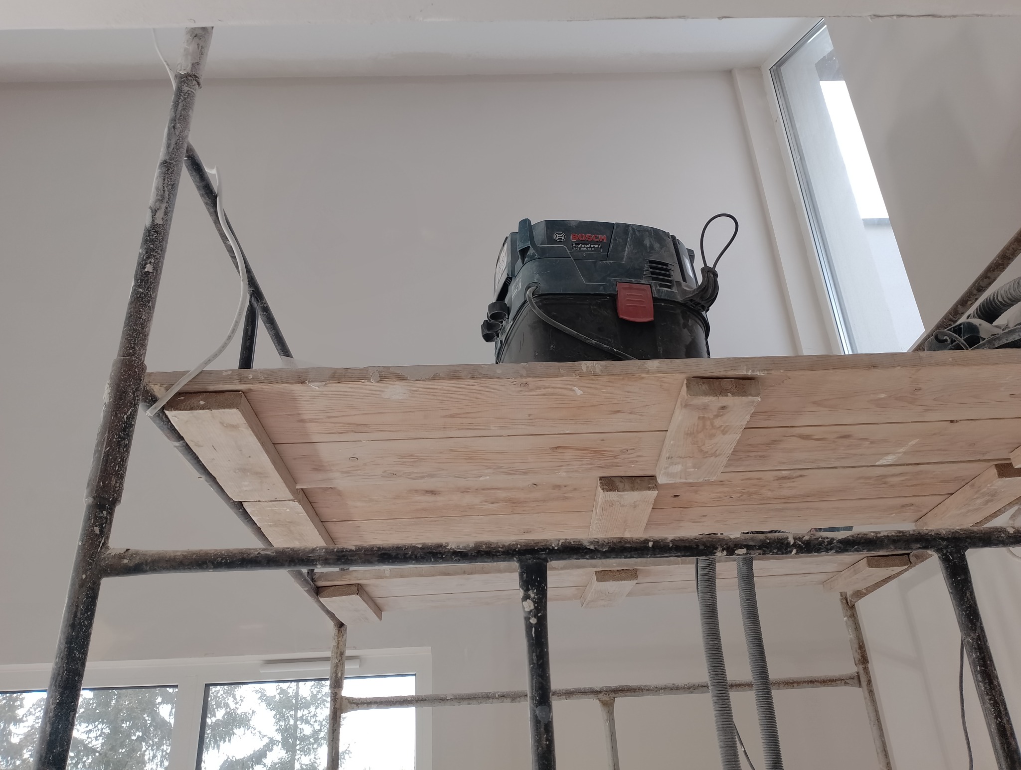 Bosch odkurzacz przemysłowy na drewnianym podeście rusztowania w trakcie prac wykończeniowych w jasnym pomieszczeniu z oknem.