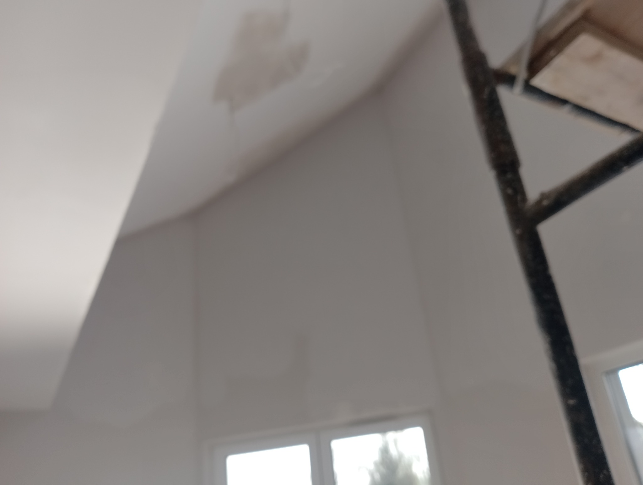 Nierównomiernie wyszpachlowany fragment sufitu pod skosem, widoczny fragment rusztowania i okna w tle.