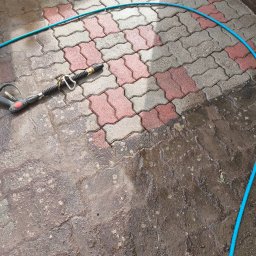 Maclin - Częściowo umyta kostka brukowa z pozostałościami brudu, wąż ciśnieniowy i pistolet natryskowy. Widoczny kontrast czystej i brudnej powierzchni.