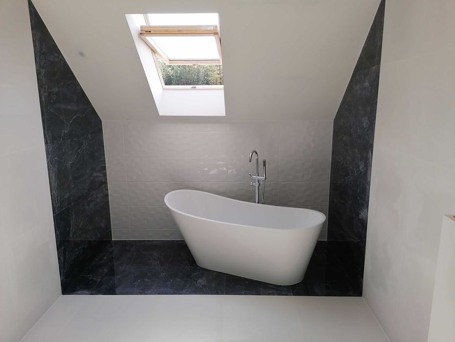 Nowoczesna łazienka na poddaszu z wolnostojącą białą wanną, armaturą w kolorze chromu, czarnymi płytkami imitującymi marmur na podłodze i ścianach oraz otwartym oknem dachowym.