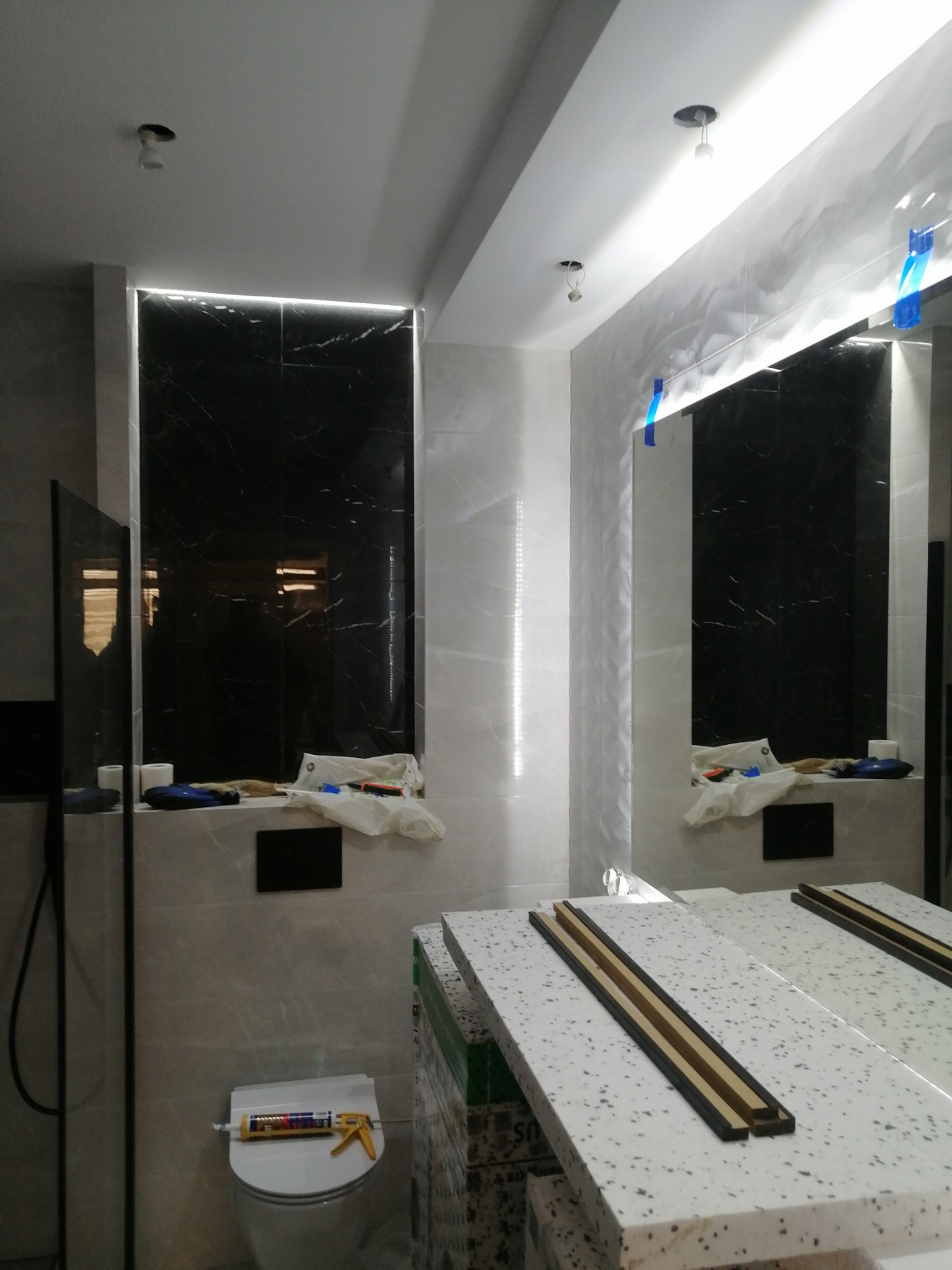 Wnętrze łazienki w trakcie remontu w Stupsku, widoczne płytki imitujące marmur, narzędzia na umywalce, silikon na sedesie i niedokończony blat pod umywalkę.