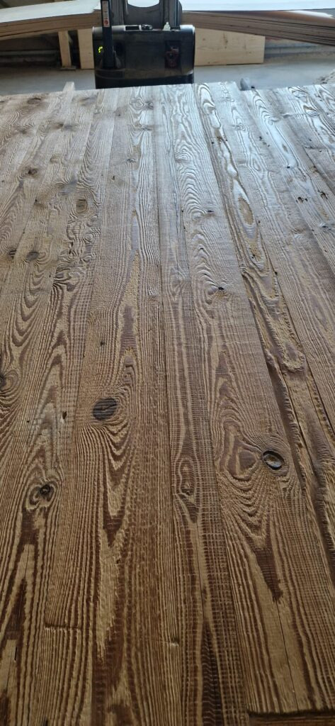 Ułożone deski z widocznym rysunkiem słojów drewna, na drugim planie wózek widłowy.