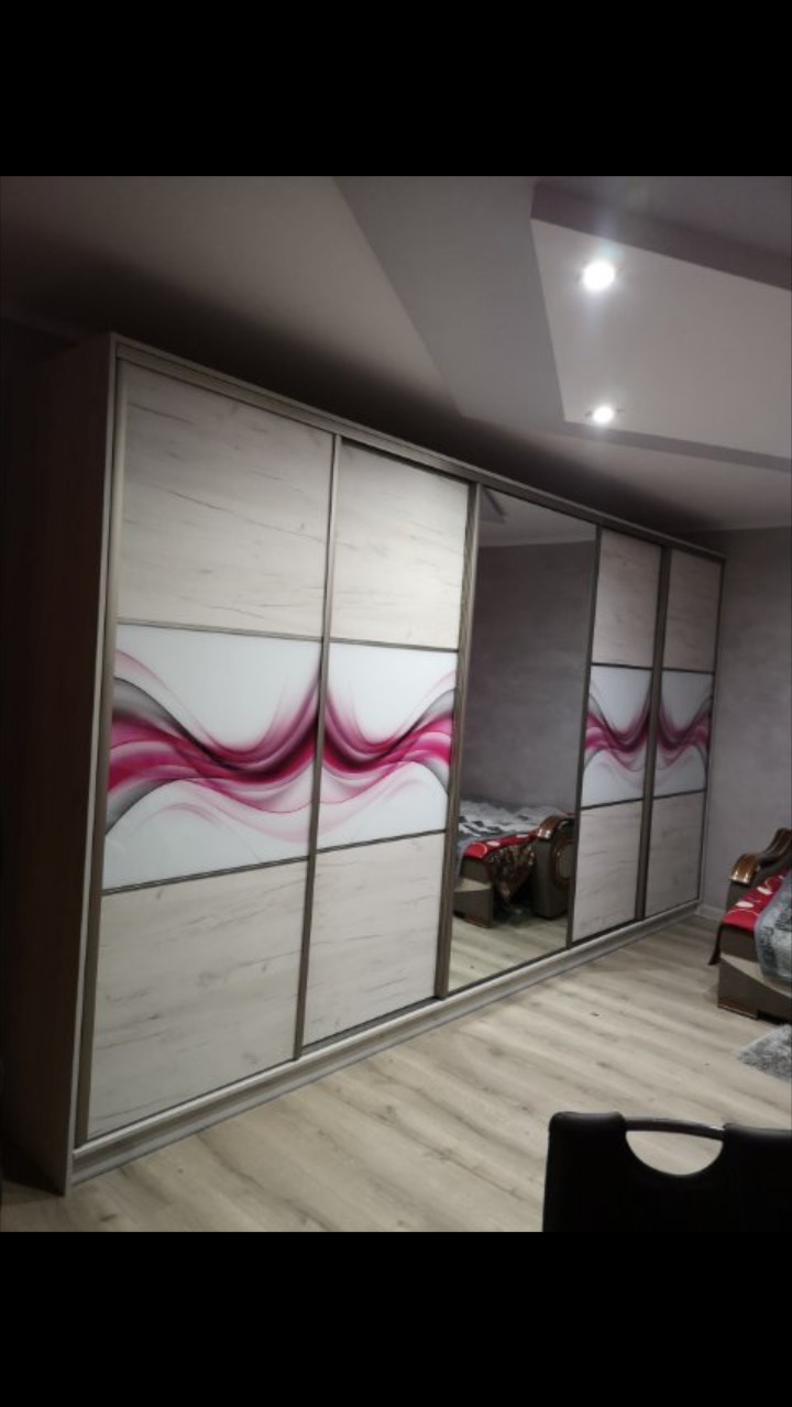 Szafa wnękowa z przesuwnymi drzwiami, dekorowana wzorem w odcieniach różu i szarości, z częściowym lustrzanym wykończeniem.