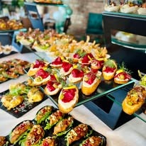 Elegancko zaaranżowane przekąski cateringowe na czarnych i przezroczystych podstawkach, widoczne kanapki z pastą, warzywami i owocami, tworzące apetyczny bufet.