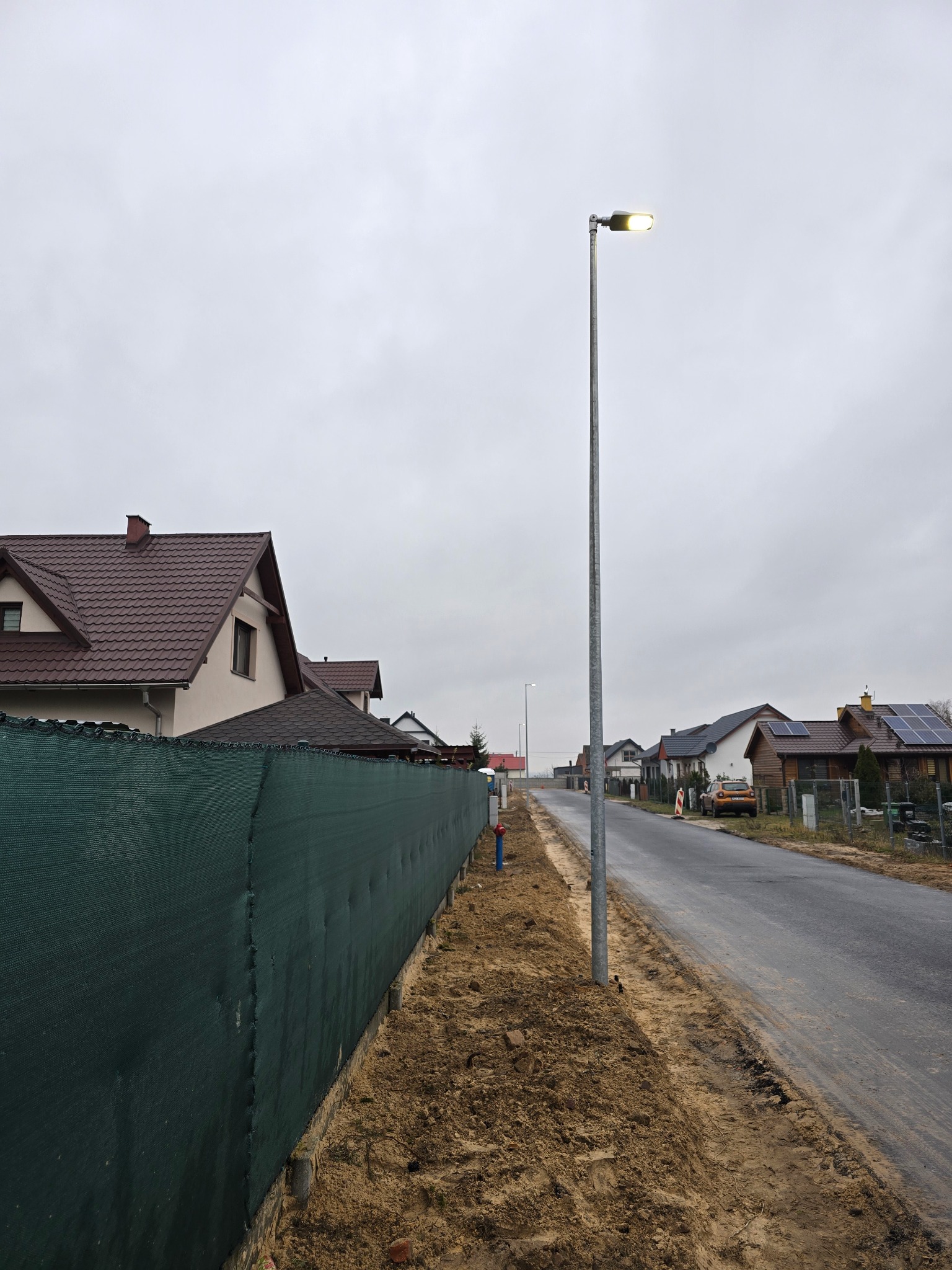 Ulica w Ujściu z nowo postawioną latarnią uliczną z energooszczędnym oświetleniem LED, widok z perspektywy chodnika.