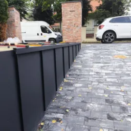 Nowoczesne obróbki blacharskie w kolorze grafitowym, z widocznymi narzędziami pracy i firmowym autem w tle. Kostka brukowa z jesiennymi liśćmi.