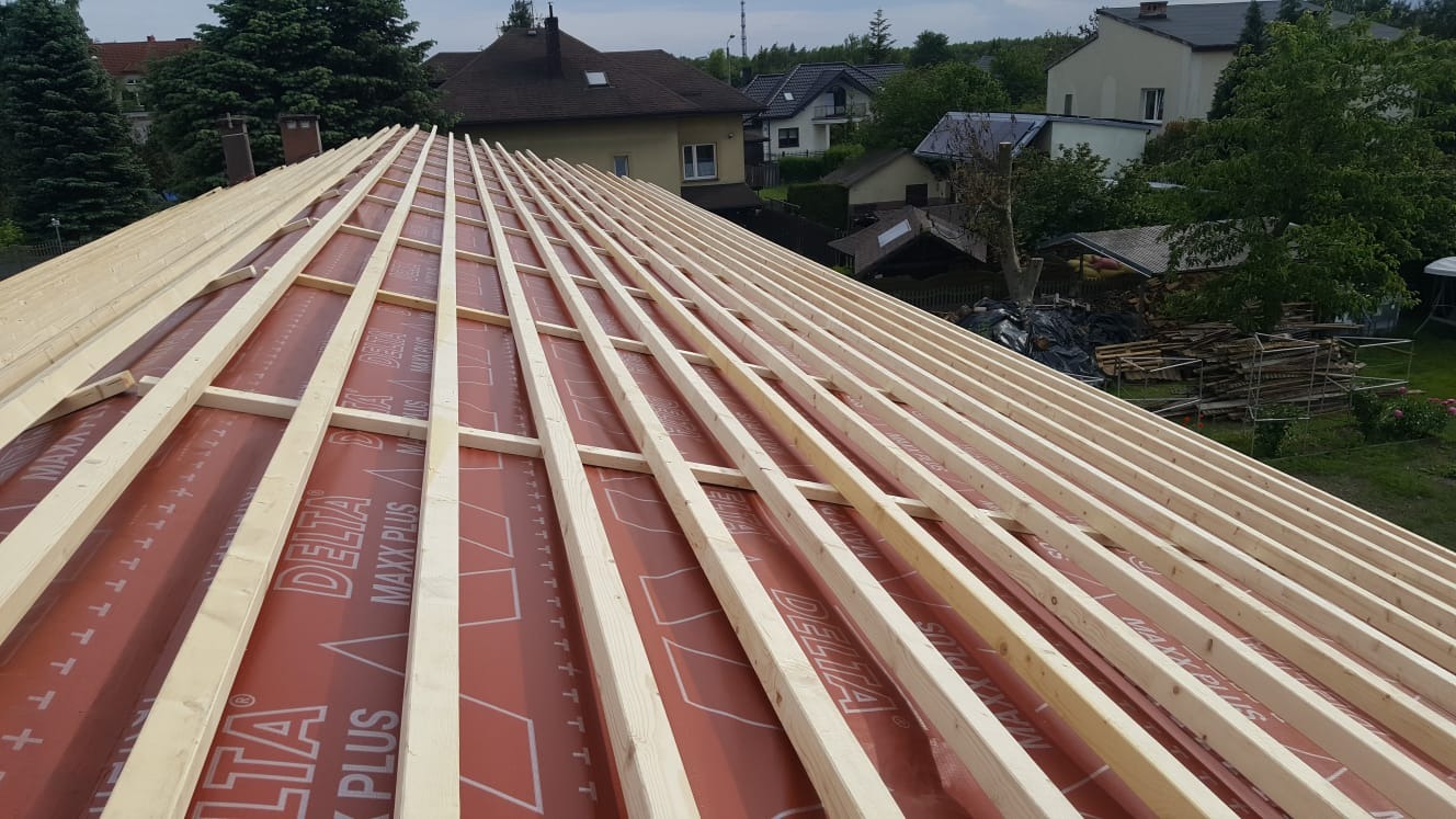 Widok z góry na konstrukcję drewnianą dachu pokrytą membraną Delta Maxx Plus, przygotowaną pod dalsze prace dekarskie, w tle zabudowa jednorodzinna i zieleń.