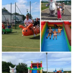 Uśmiechnięty mężczyzna i dzieci bawią się na dmuchanym, pomarańczowym robaku na zielonym boisku, obok dmuchany zamek ze zjeżdżalnią, pluszowy królik w tle, impreza plenerowa.