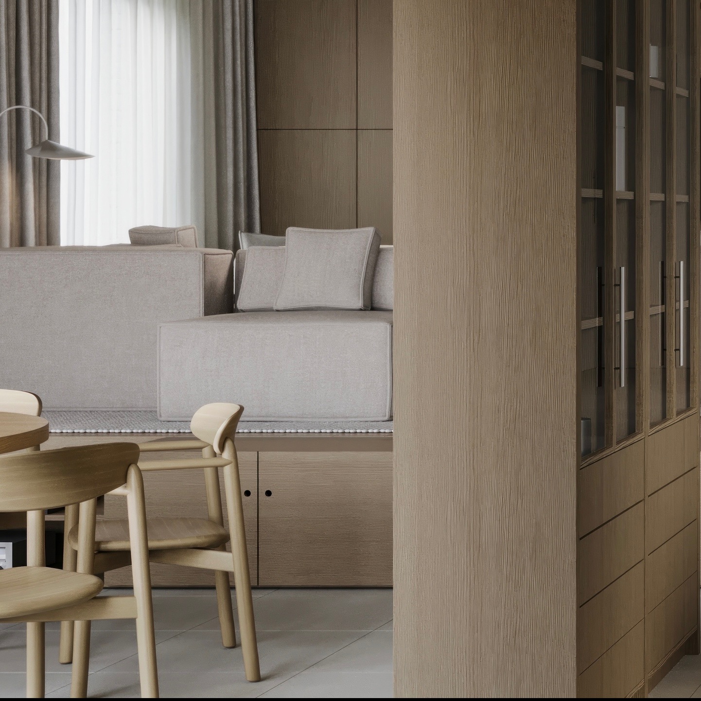 Jasna aranżacja wnętrza: minimalistyczny salon z drewnianymi krzesłami przy okrągłym stole, modułowa sofa z poduszkami i zabudowana szafa z przeszklonymi drzwiami.