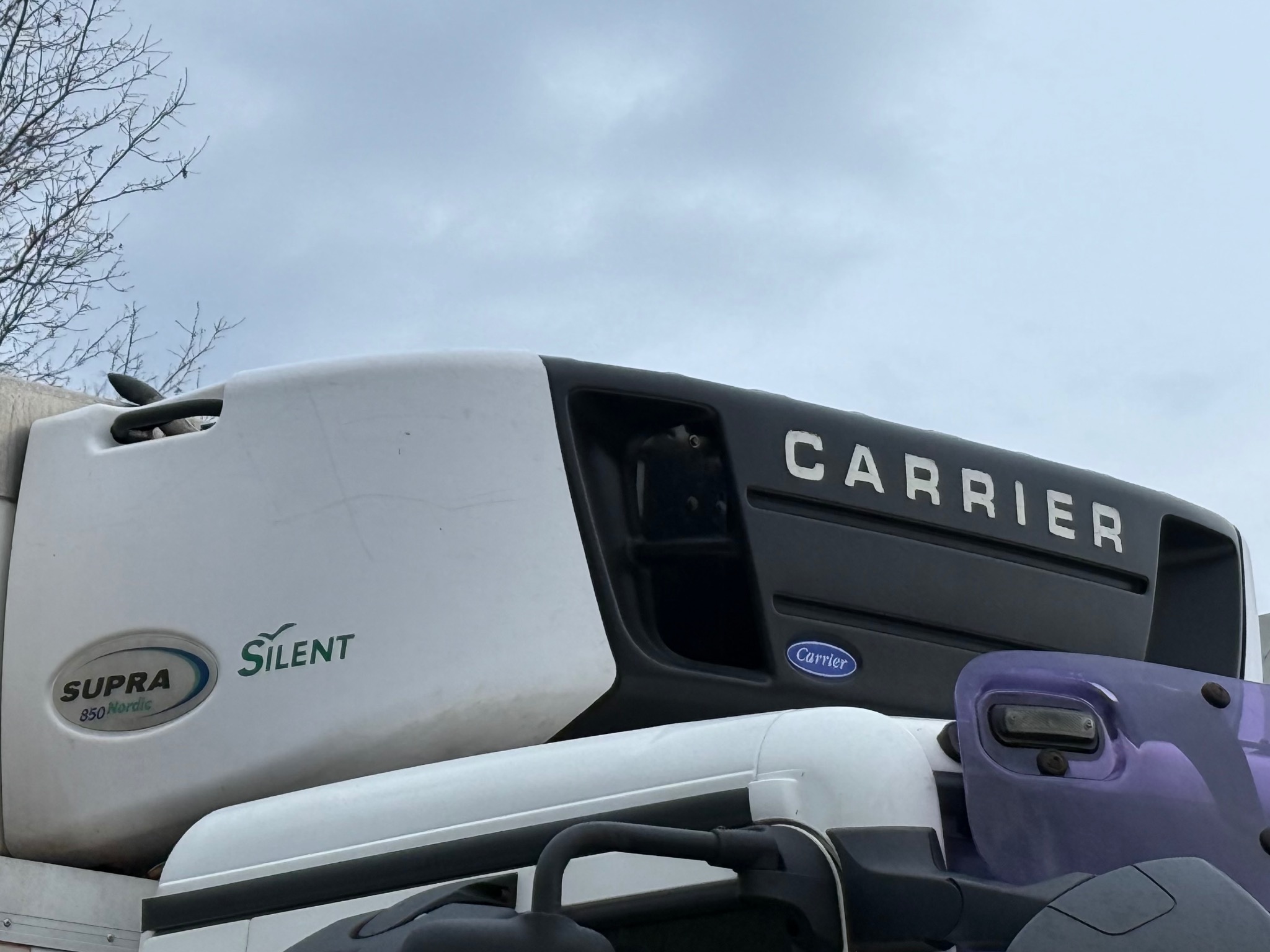 Agregat chłodniczy Carrier Supra 850 Nordic Silent na ciężarówce, widok z dołu na tle pochmurnego nieba. Detal transportu chłodniczego.