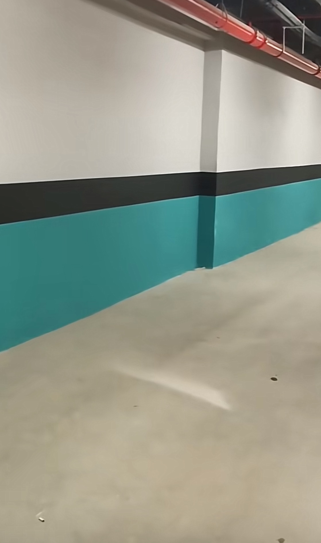 Wnętrze garażu podziemnego po malowaniu ścian na biało, turkusowo i czarno, z widocznymi rurami instalacji pod sufitem.