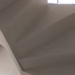 Usługi Ogólnobudowlane Paweł Soboń - Betonowe schody spiralne w jasnym wnętrzu, widok z góry, z wiadrem malarskim w rogu.