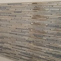 Mozaika ścienna z wąskich, poziomych płytek w odcieniach szarości, srebra i bieli, z elementami o metalicznym połysku i zróżnicowanej fakturze, ułożona na ścianie w łazience.