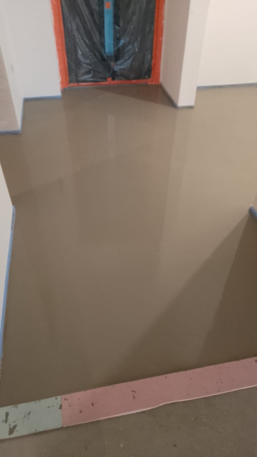 Świeżo wylana, samopoziomująca wylewka podłogowa w Głoskowie, przygotowana pod dalsze prace wykończeniowe, z widocznym zabezpieczeniem folią drzwi i listwami piankowymi przy ścianach.