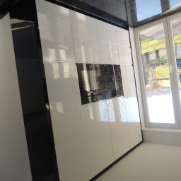 STUDIO RS MEBLE NA WYMIAR - Biała szafa wnękowa z połyskiem, czarne obramowanie, zabudowa pod sufit, widoczne okno z odbiciem drzew