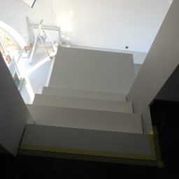 STUDIO RS MEBLE NA WYMIAR - Nowoczesne, białe schody z widocznymi taśmami malarskimi zabezpieczającymi podłogę, w tle okno łukowe i drabina malarska.
