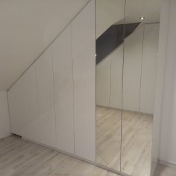 STUDIO RS MEBLE NA WYMIAR - Biała szafa wnękowa z lustrzanymi drzwiami, dopasowana do skosu poddasza, widoczne odbicie podłogi w lustrze.