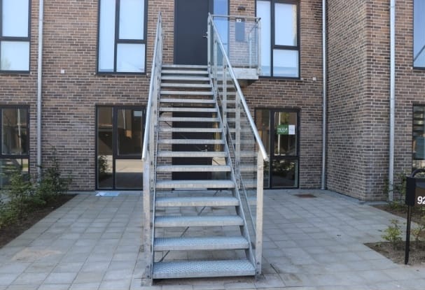 Zewnętrzne schody metalowe z przezroczystą balustradą prowadzące do drzwi na piętrze w nowoczesnym budynku z cegły.