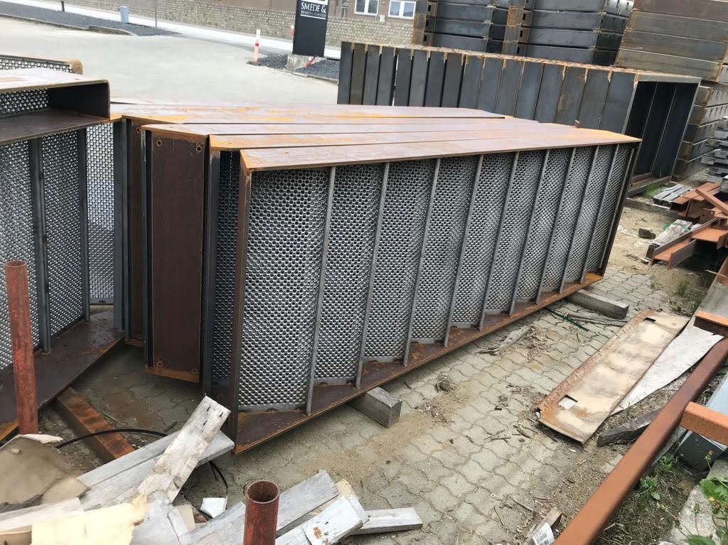 Metalowe elementy konstrukcyjne z perforowaną siatką, prawdopodobnie fragmenty ogrodzenia, składowane na zewnątrz.