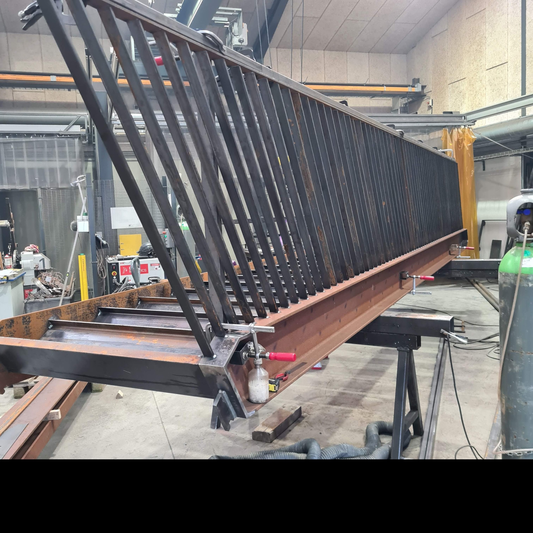 Konstrukcja metalowa balustrady w warsztacie, widoczne spawy, uchwyty mocujące i narzędzia, surowy stan przed obróbką i malowaniem.