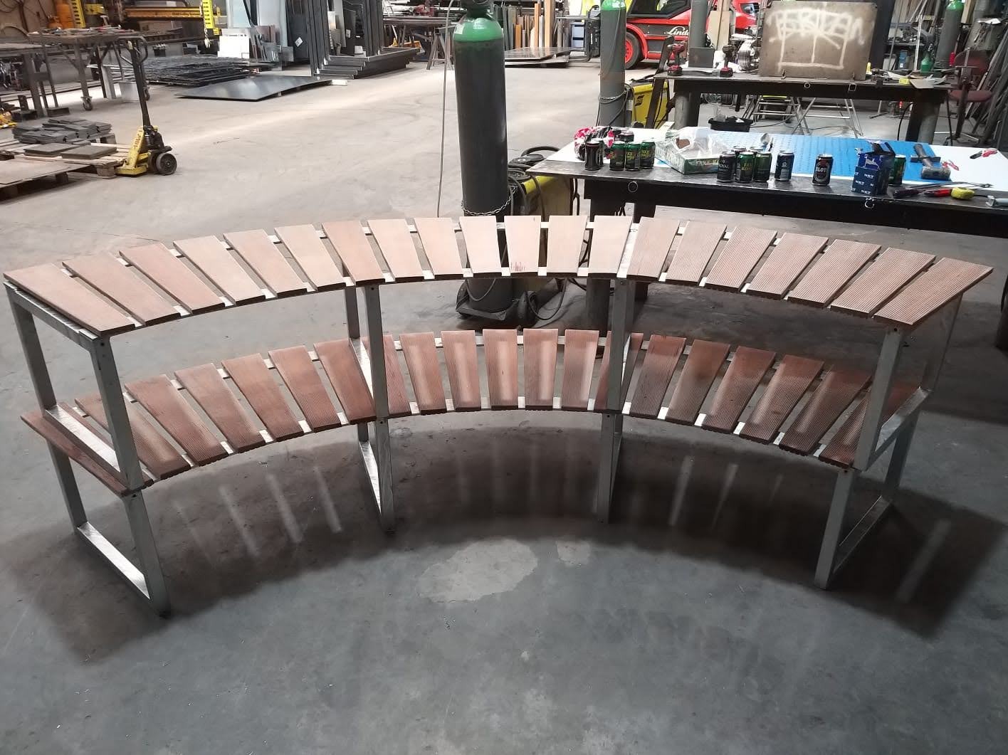 Dwu-poziomowa, półokrągła konstrukcja z metalowym stelażem i drewnianymi listwami, prawdopodobnie element wyposażenia ogrodu lub tarasu, widoczna w warsztacie.