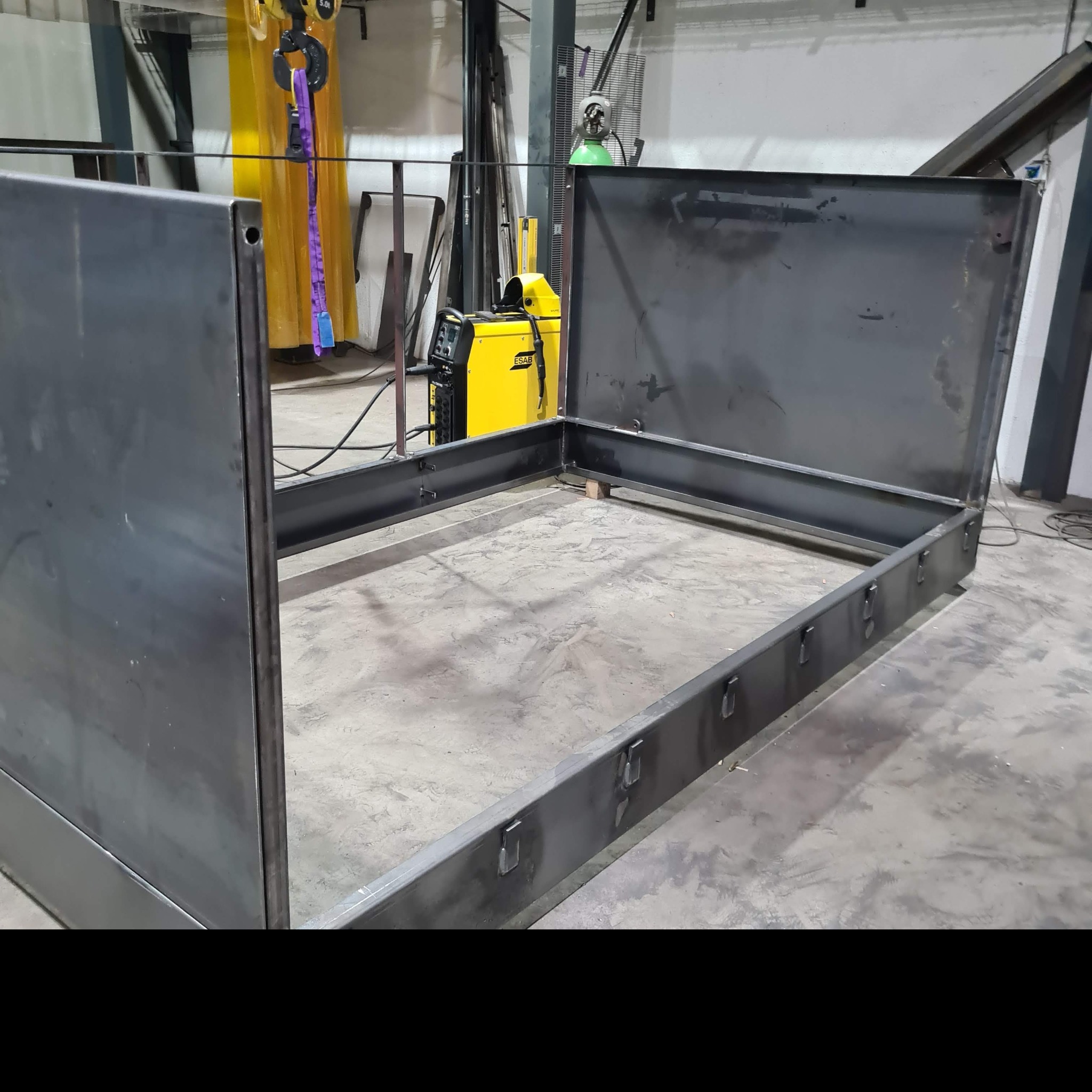 Rama łóżka metalowego w trakcie spawania, widoczny spawarka ESAB, surowy metal, warsztat.