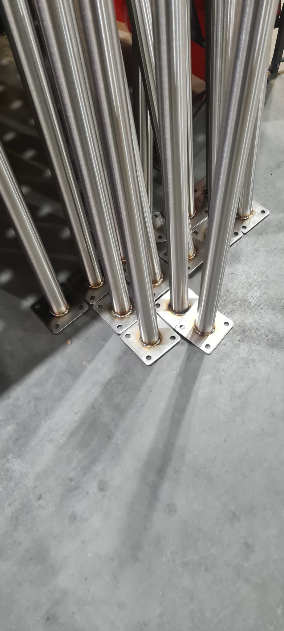 Przygotowane do montażu słupki poręczy ze stali nierdzewnej z przyspawanymi podstawami, widoczne spawy, Kielno.
