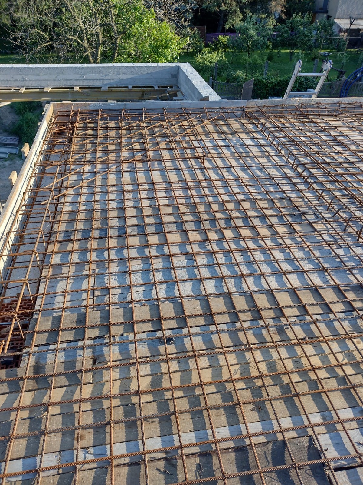 Zbrojenie płyty fundamentowej z widocznymi deskami szalunkowymi i betonowymi ścianami w tle, widok z góry.