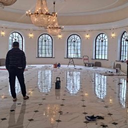 Artur Tudek wykończenia wnętrz usługi malarskie ,glazurnicze - Przestronne, okrągłe wnętrze z marmurową podłogą w trakcie prac wykończeniowych; widoczne narzędzia, resztki zaprawy i dwóch mężczyzn w tle.