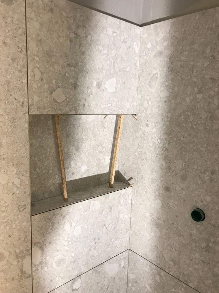 Wnęka prysznicowa wyłożona szarymi płytkami imitującymi lastryko, podparta drewnianymi listwami na etapie montażu.