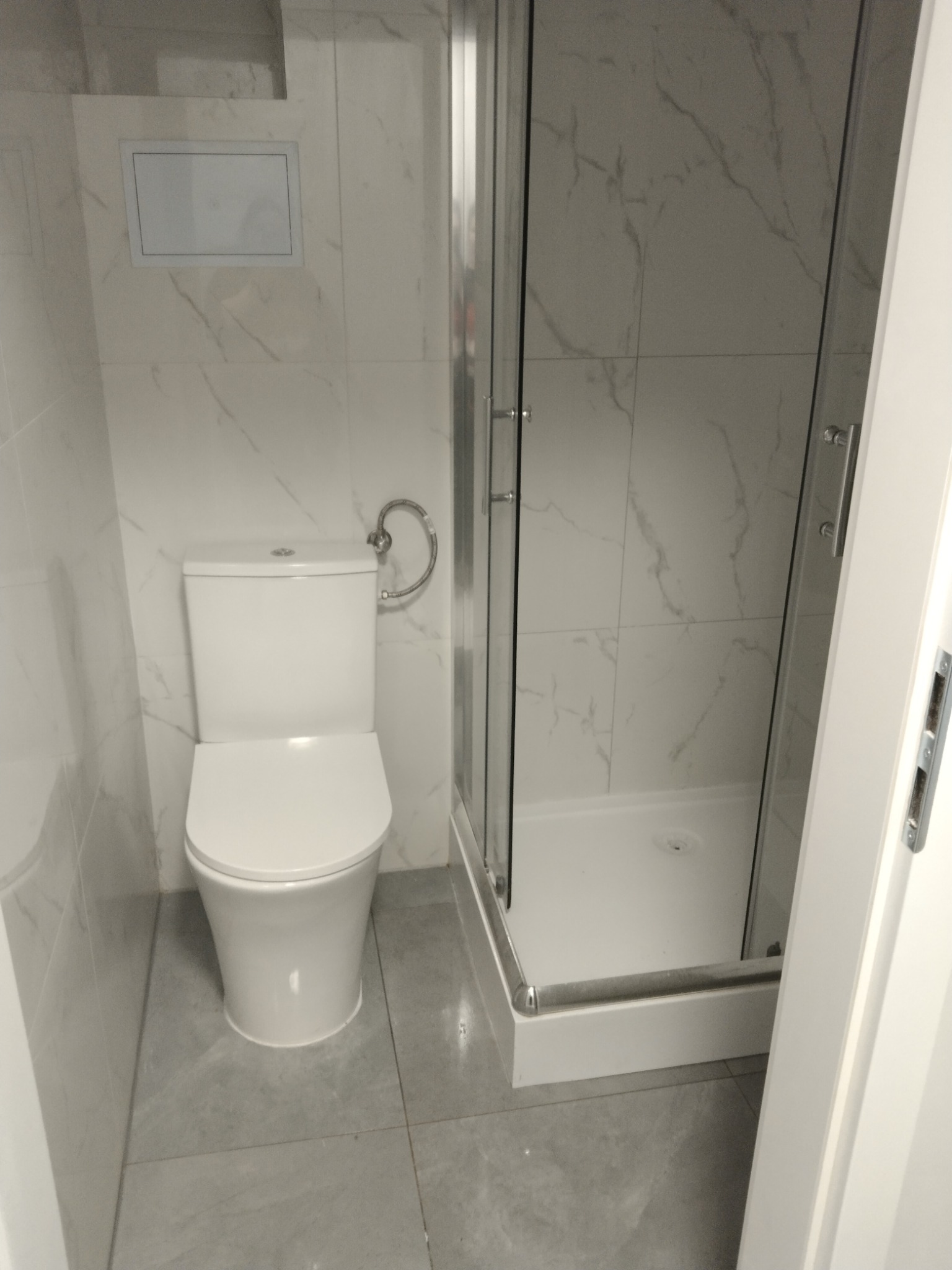 Wykończona łazienka w Koszalinie z białą toaletą i kabiną prysznicową z marmurowymi płytkami na ścianach i szarymi płytkami na podłodze.