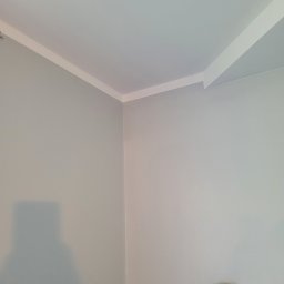 Krystian Gula - Świeżo pomalowane wnętrze w odcieniach szarości z białym wykończeniem sufitu i włącznikiem światła na ścianie.