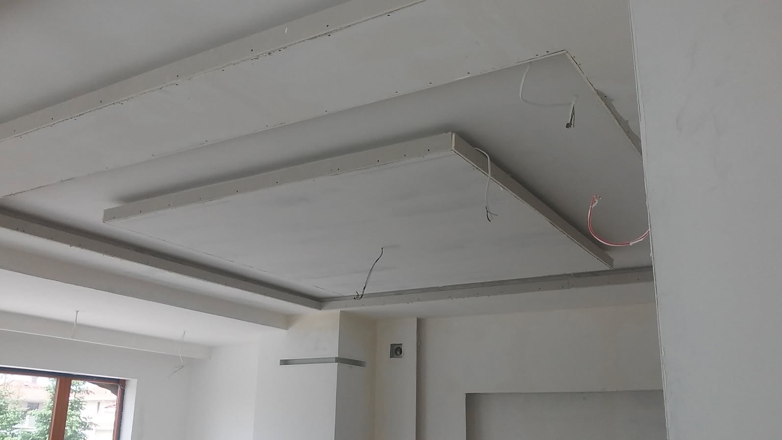 Sufit podwieszany z płyt kartonowo-gipsowych w trakcie montażu, widoczne przewody elektryczne i elementy konstrukcyjne, surowe wykończenie ścian.
