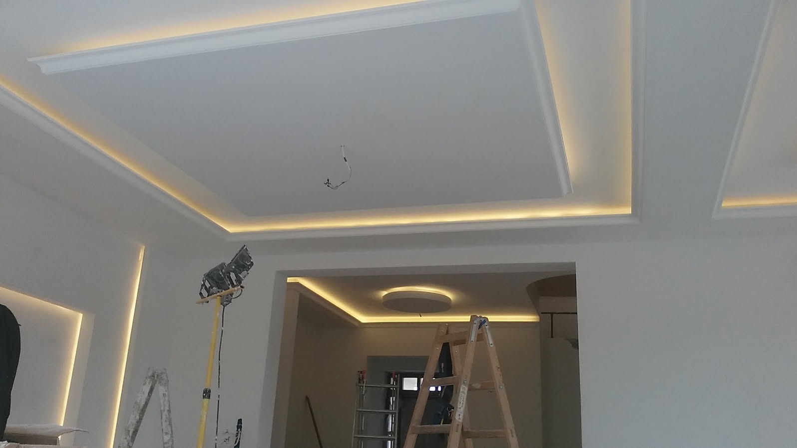 Wykończony sufit podwieszany z oświetleniem LED w nowocześnie urządzonym wnętrzu, widoczna drabina i lampa robocza.