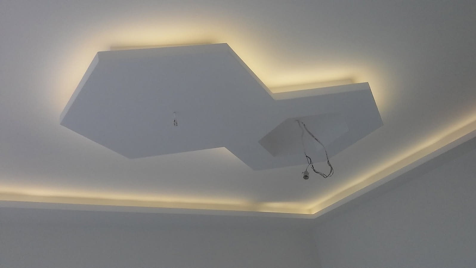 Nowoczesny sufit podwieszany z płyt kartonowo-gipsowych o nieregularnym kształcie, z oświetleniem LED wzdłuż krawędzi, widoczne przewody elektryczne w oczekiwaniu na montaż oświetlenia.