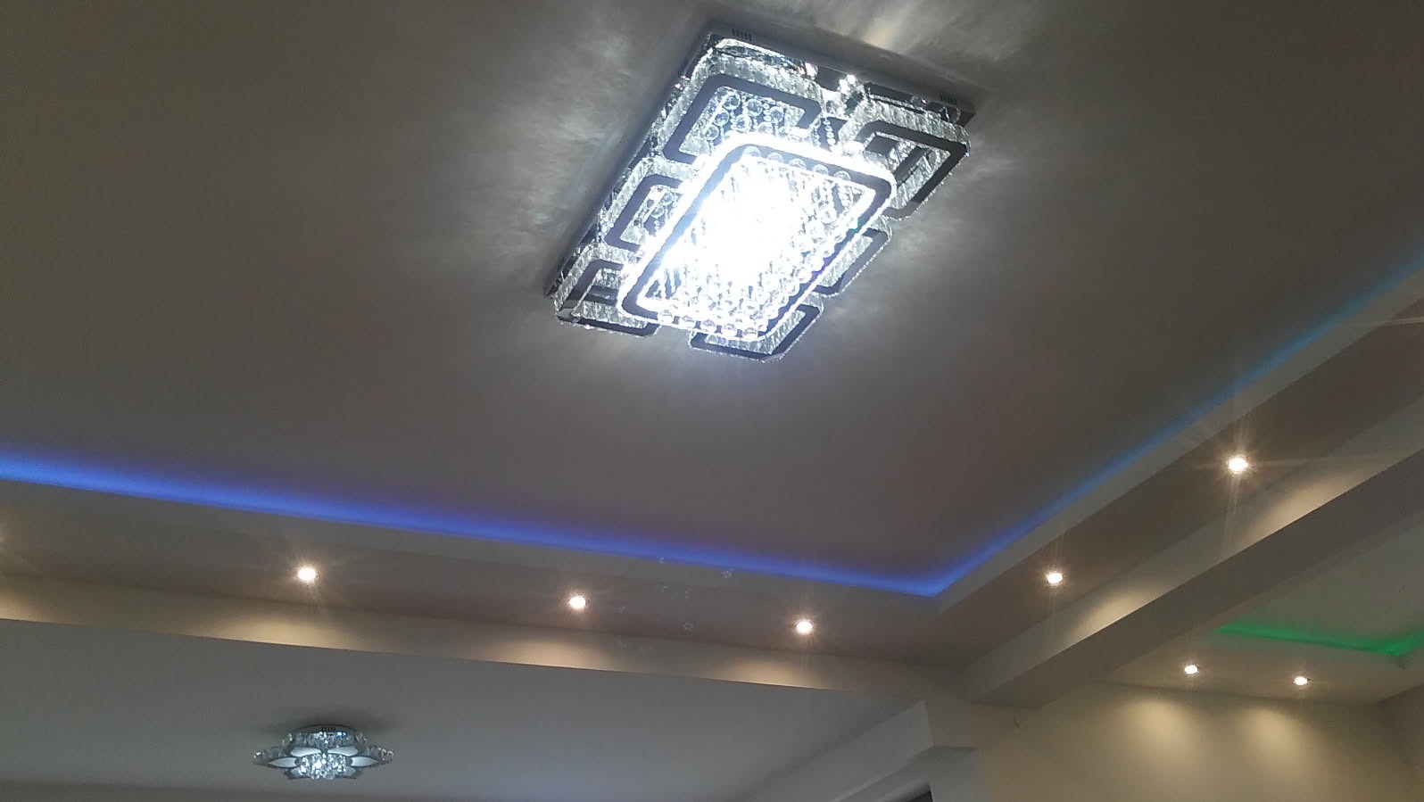 Sufit podwieszany z oświetleniem LED w kolorze niebieskim i zielonym oraz dwa ozdobne żyrandole kryształowe.