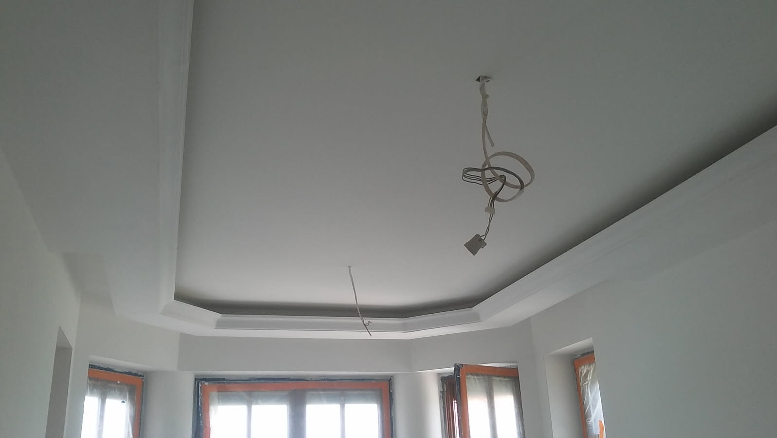 Pomieszczenie po malowaniu na biało, widoczne listwy dekoracyjne pod sufitem i wystające kable elektryczne.