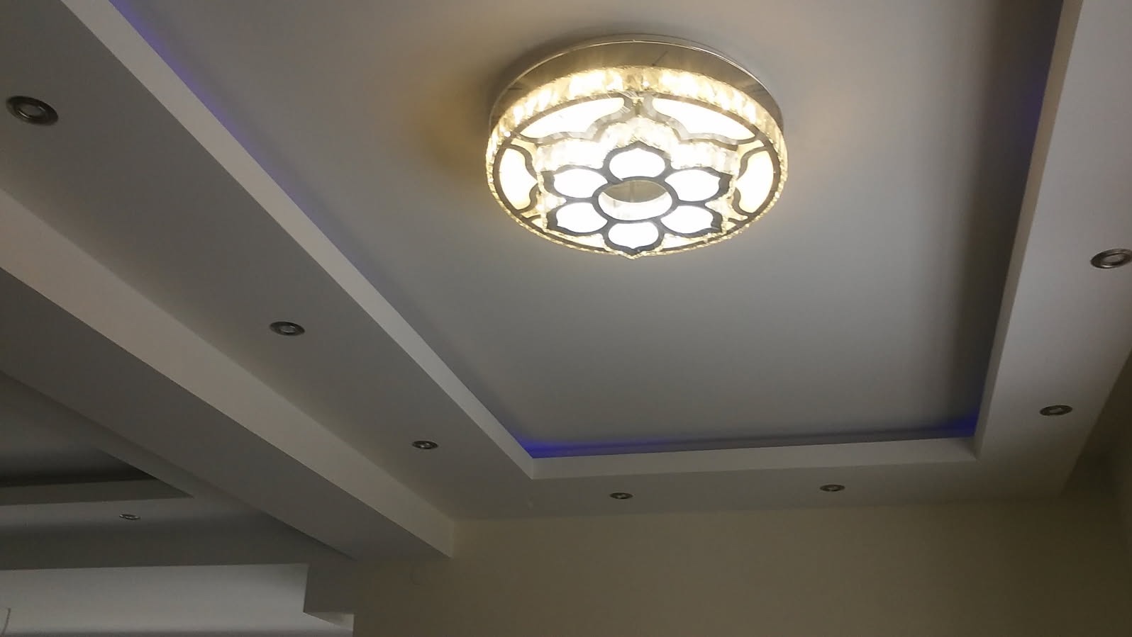 Dekoracyjny sufit podwieszany z oświetleniem punktowym i centralnym żyrandolem w kształcie kwiatu, podświetlenie LED w kolorze niebieskim.